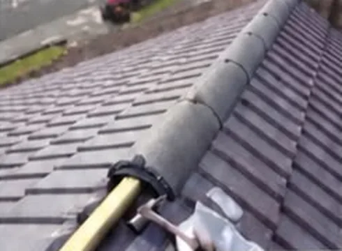 Ridge tiles on a grey tiled roof being repointed by a roofer